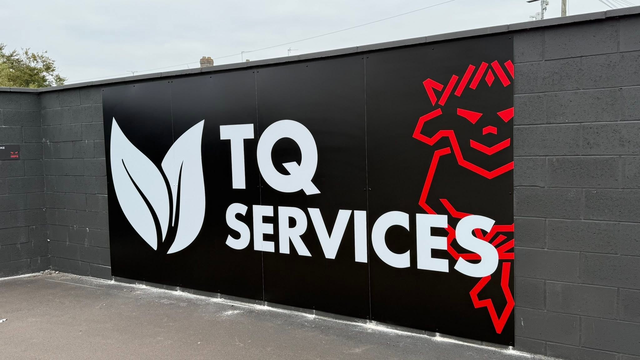 Large TQ Services wall sign installed by GRS Signs, featuring a white leaf logo, company branding and a red Lincoln City FC Imp graphic on a black background.