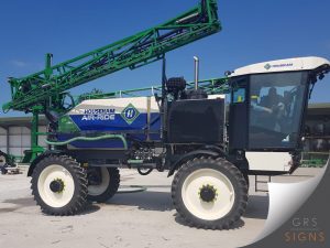 Custom livery for a Househam Air-Ride AR4 agricultural sprayer, featuring the company's signature blue, white, and green colour scheme. The design incorporates a bold blue lower section, white upper tank panels, and green geometric accents, with prominent Househam Air-Ride branding and logo displayed on the side. The clean, professional graphics complement the machine's industrial form while creating strong brand visibility in agricultural environments.