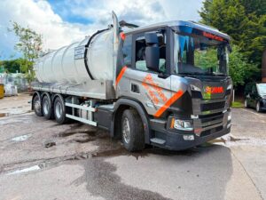 Vehicle livery for Blockfree Services on a grey Scania vacuum tanker featuring bold orange branding, illuminated company graphics and professional fleet vehicle signage. The design incorporates bright orange and grey branding graphics applied to the cab, illuminated company branding on the front grille and digital destination display, with a large white tanker mounted behind the cab.