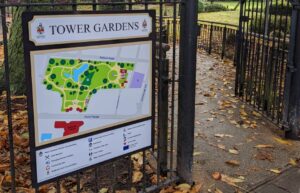 Freestanding park information and wayfinding sign for Tower Gardens, mounted to decorative black metal railings.