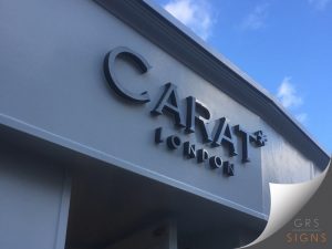 3D cut out black lettering projecting from its exterior wall background. The word "CARAT*" is displayed in a serif style font, with "LONDON" underneath it, smaller and in a sans-serif style font. The angle of the photograph shows the depth of the lettering.