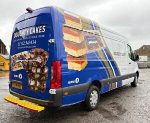 Vehicle livery for Doughty Cakes on a blue Mercedes Sprinter van featuring full-colour cake imagery, company branding, website details and bespoke commercial vehicle graphics.