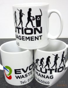 Set of three white ceramic promotional mugs branded for Evolution Waste Management. The mugs feature a bold black logo and typography, incorporating an evolutionary-style silhouette graphic transitioning into a figure disposing of waste in a recycling bin. The company name and contact details are printed on the mugs, alongside a colourful circular logo.