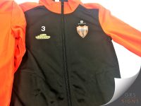 Custom branded sports jacket featuring a black body with bright orange sleeves and shoulder panels. The jacket is personalised with a white number 3, the Ultimate logo, and a club crest printed on the chest. A full-length black zip runs down the centre, while the contrasting orange and black colour scheme creates a smart and professional appearance suitable for teamwear, training, or sports club apparel.