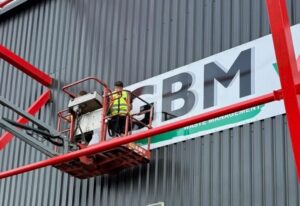 Installation of a GBM Waste Management fascia sign by GRS Signs at Lincoln City Football Club, showing engineers fitting external branded signage to the stadium exterior.