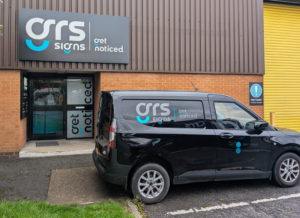 Front entrance of GRS Signs featuring branded signage above the entrance and a company vehicle parked outside the building.