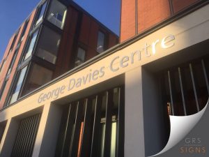 A building entrance showing cut-out, large lettering in a brushed metallic material and 3D-style, to identify George Davies Centre.
