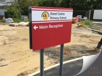 A dual-post, double-sided wayfinding sign for Great Coates Primary School, designed to direct visitors to the Reception area. The sign features a bold red background with clear white lettering for maximum visibility and readability. The school's name and crest are displayed within a separate white header panel, creating strong contrast and enhancing the prominence of the branding.