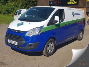 White Ford Transit Custom van featuring a clean and professional vehicle livery for Househam. The design incorporates the company's signature blue lower bodywork, a bold green stripe running along the sides, and prominent Househam logos displayed on the bonnet and side panel.