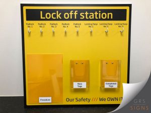 Bright yellow lock-off station board designed for workplace safety and maintenance procedures. The board features labelled hooks across the top for five padlocks and three locking hasps, with clear headings identifying each position. Three transparent storage pockets are mounted below, labelled Procedure, New Tags, and Completed Tags. Bold black text at the top reads "Lock off station", while the bottom of the board displays the safety slogan "Our Safety /// We OWN IT". The 'safety yellow' and black colour scheme ensures the station is easily identifiable in its environment.