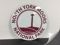 A circular road sign, white with burgundy text/elements, reading "NORTH YORK MOORS NATIONAL PARK"