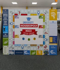 Bespoke educational wall display designed as a custom "University Houseopoly" board game. The large modular sign features colourful game-board-style panels, house points information, school values, rewards and behaviour guidance, creating an engaging and interactive display for a school environment.