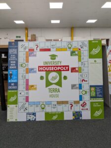 Bespoke educational wall display designed as a custom "University Houseopoly" board game. The large modular sign features colourful game-board-style panels, house points information, school values, rewards and behaviour guidance, creating an engaging and interactive display for a school environment.