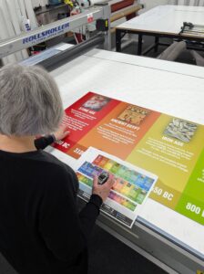 A team member carries out a quality check on a large educational timeline graphic before production.