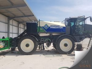 Side view of a Househam Predator self-propelled agricultural sprayer featuring the company's distinctive blue, white, and green livery. Large Househam Predator branding is displayed prominently on the side-mounted tank, with angled green graphics incorporating the Househam logo.