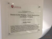 Transparent acrylic donor plaque mounted with four metal stand-off fixings, displaying the University of Leicester crest and logo. The plaque is mounted on a light-coloured interior wall. The plaque thanks donors to the Wladyslaw Sluckin Memorial Fund and the Sluckin family for supporting the building of the Sluckin Room.