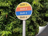 Circular shift identification sign mounted on a silver post, featuring four horizontal colour-coded bands labelled Shift 1, Shift 2, Shift 3, and Shift 4. The design uses soft yellow, orange, blue, and cream sections, with bold contrasting text ensuring each shift is clearly distinguishable.