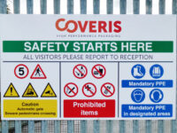 Large health and safety information sign for Coveris High Performance Packaging, displayed on perimeter fencing at a site entrance. The sign features a bold green header reading "SAFETY STARTS HERE", followed by instructions directing all visitors to report to reception. A series of coloured safety symbols provide information on site speed limits, pedestrian crossings, automatic gate hazards, prohibited items, and mandatory PPE requirements, including safety footwear, high-visibility clothing, hearing protection, and head protection in designated areas. The white background, clear iconography, and colour-coded sections create a highly visible and easy-to-understand workplace safety sign. The sign is mounted to a metal railing fence.