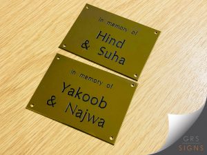 Engraved brass memorial plaques with drilled, circular fixing holes. "In memory of Hind & Suha" and "In memory of Yakoob & Najwa".