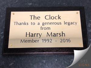 Brass plaque fixed to a wooden frame. Engraved black lettering reads "The Clock, Thanks to a generous legacy from Harry Marsh, Member 1992-2016".