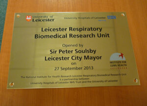 A close up of an engraved, brass plaque with drill holes and logos for The University of Leicester.