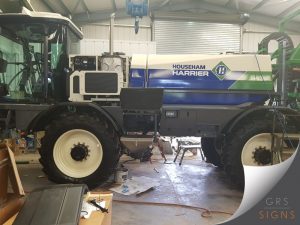 Side view of a Househam Predator self-propelled agricultural sprayer featuring the company's distinctive blue, white, and green livery. Large Househam Predator branding is displayed prominently on the side-mounted tank, with angled green graphics incorporating the Househam logo.