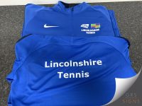 Customised Lincolnshire Tennis training apparel consisting of matching blue quarter-zip sports tops. The garments feature a vibrant royal blue colour with contrasting black shoulder panels and white printed branding. A white Nike swoosh is positioned on the chest alongside the LTA British Tennis logo, while "Lincolnshire Tennis" is printed prominently in bold white lettering across the back.