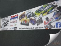 Large printed banner for Louth Radio Control Car Club (Louth RCCC) featuring photographs of radio-controlled racing cars, club members, and track action. The design displays the BRCA (British Radio Car Association) logo alongside sponsor logos including Schumacher Racing, and promotes the club website www.louthrccc.co.uk. Bold text encourages visitors to "Join us on Facebook!", while the dynamic layout combines motorsport imagery, club branding, and sponsor graphics to create an eye-catching promotional display for the RC car racing club.