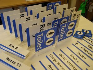 NHS Flag signs with a base-plate mount. These are double-sided so can be read from either direction. The signs shown are for wayfinding and room identification.