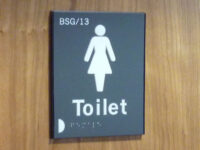 A close up of a tactile and braille "toilet" sign for female toilets, including a room number