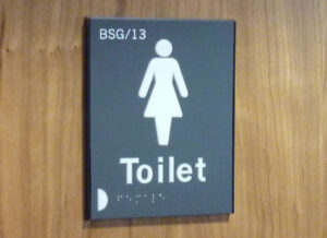A close up of a tactile and braille toilet sign for female toilets, including a room number