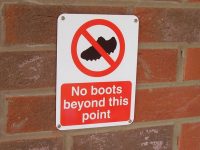 Wall mounted aluminium warning sign on outside wall that reads "no boots beyond this point"