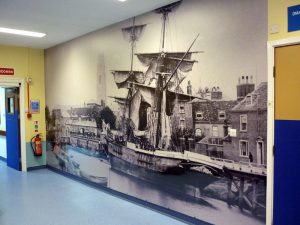 Large wall art covering the entirety of a wall, featuring a black & white historical photo of a large ship and houses.
