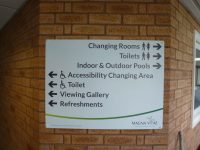 Fixed aluminium wayfinding sign on external wall, featuring company logo for Magna Vitae.