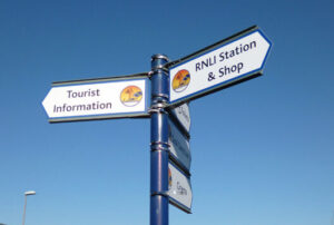 A cantilever fingerpost sign in Mablethorpe aiding wayfinding for the RNLI station, shop, and local attractions.