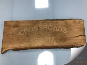 An engraved, rustic, natural wooden sign that reads "Crossroad Farms".